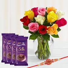 Multicoloured roses in a vase, paired with decorative Rakhi and chocolate