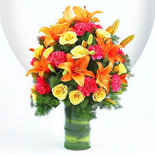 Pink Carnations, Orange Lilies, and Yellow Roses fused together in a glass vase.